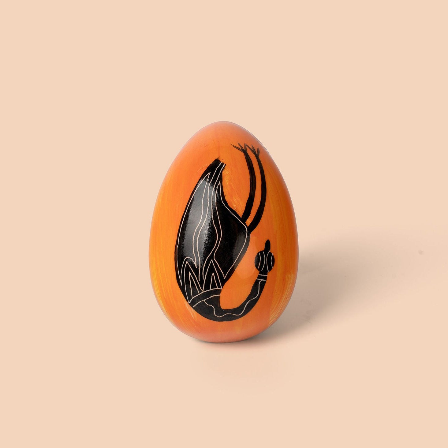 Orange egg-shaped object with black design on a beige background